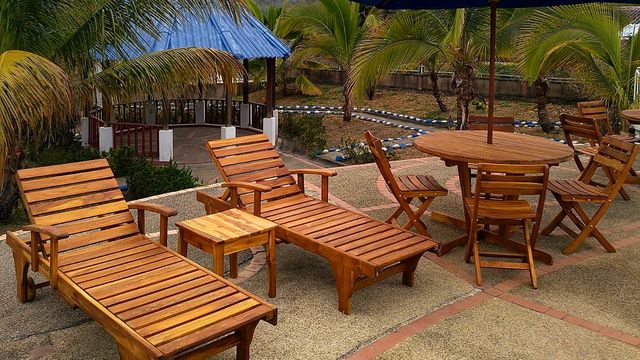 Asoleadoras de madera, mesa y parasol azul entre palmeras en Hotel Cabaleón, Tena